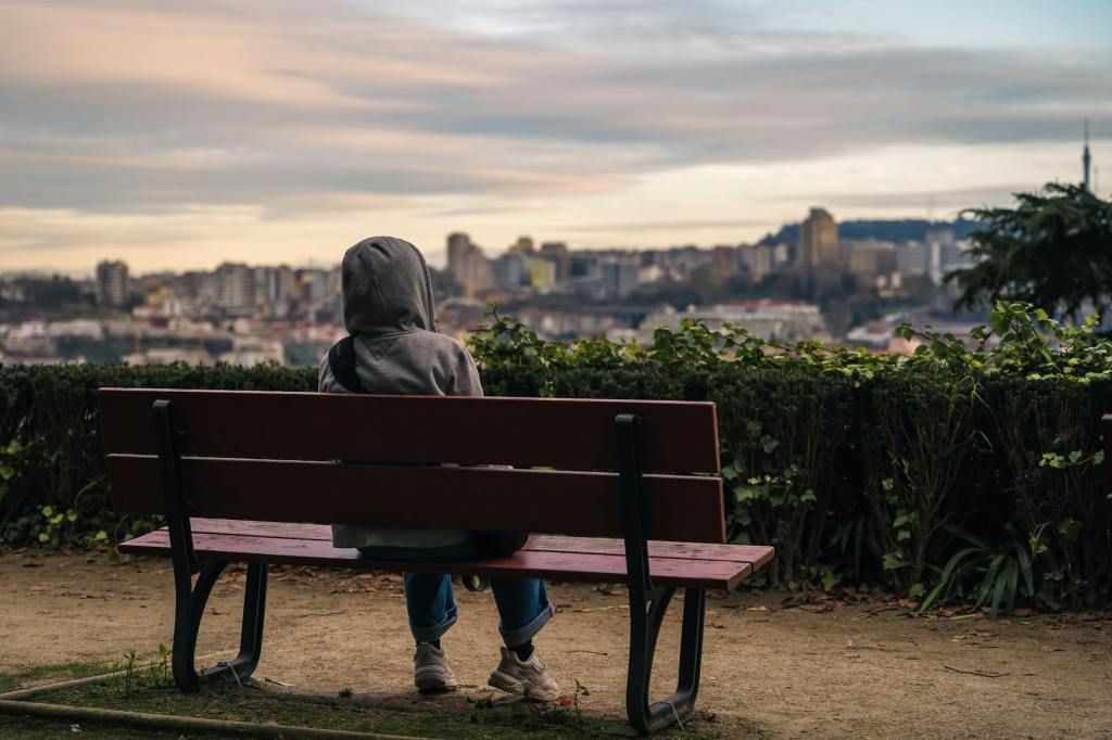 person in hood sitting on bench at park